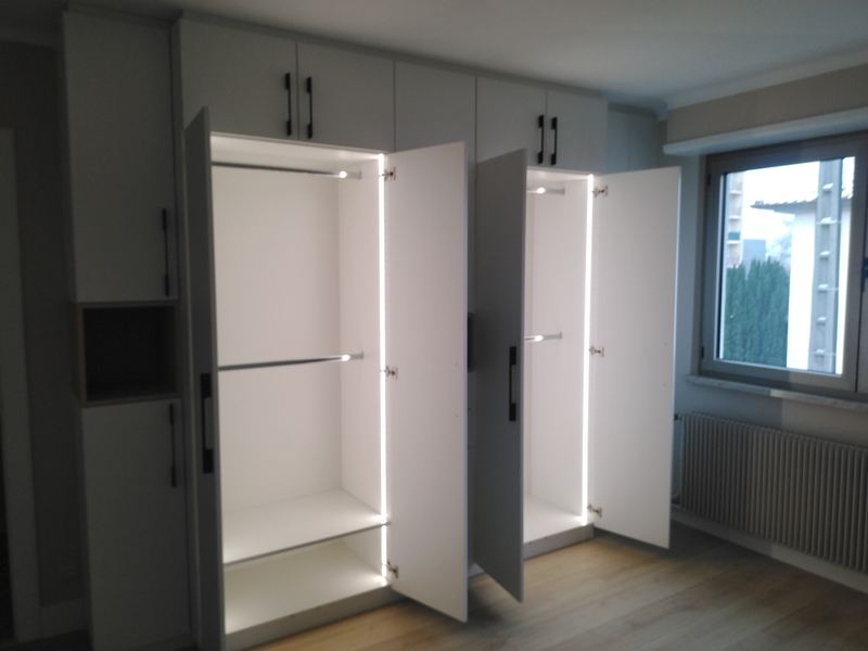 Armoire blanche toute hauteur, deux portes ouvertes sur un intérieur blanc éclairé par des LED verticales avec tringles