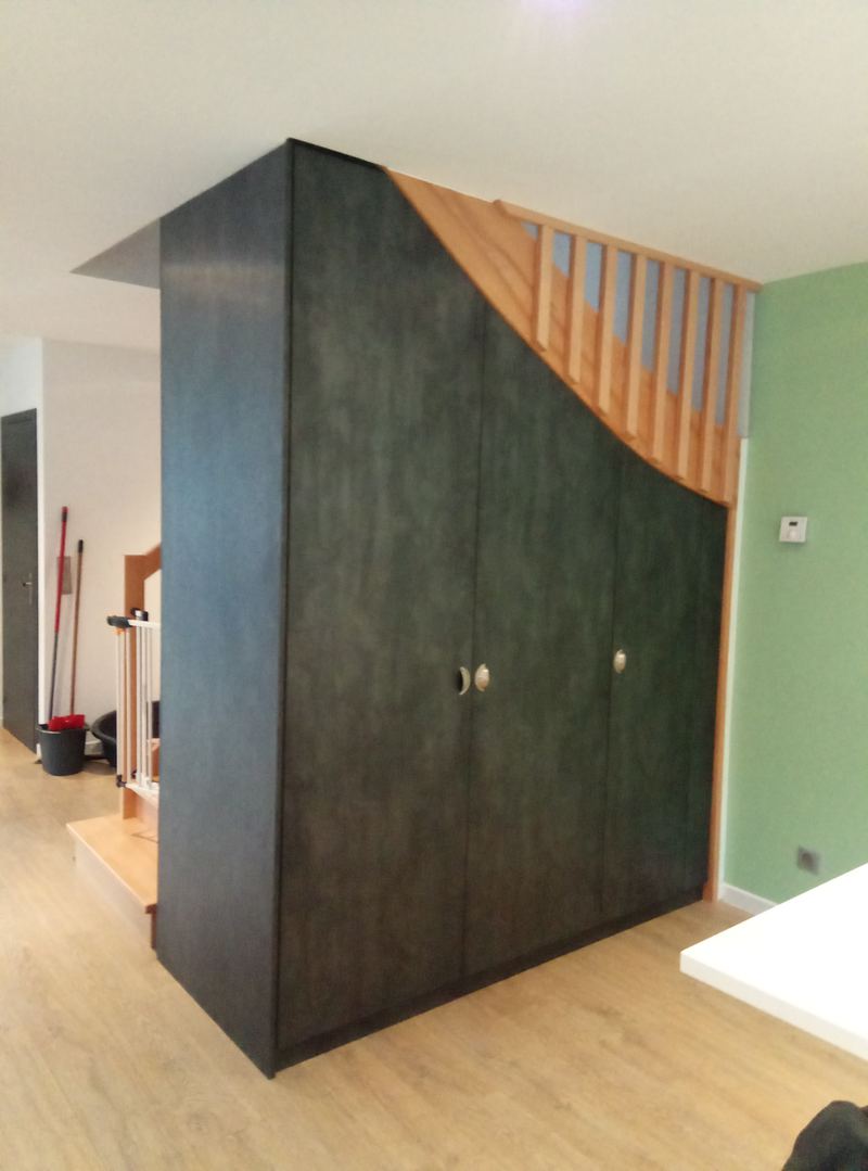 Le même ensemble fermé : grande armoire sombre (décor ardoise) épousant la pente de l'escalier bois, boutons ronds