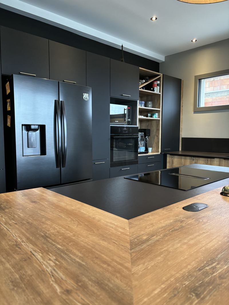 Îlot à plan de travail noir mat et retour en décor bois au premier plan, plaque induction