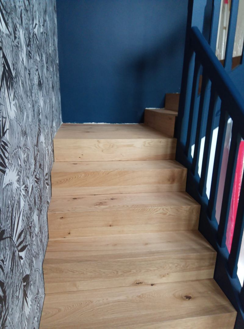 Escalier habillé de marches et contremarches en chêne massif clair, garde-corps à barreaux peints bleu nuit, mur bleu nuit et papier peint à feuillage noir et blanc