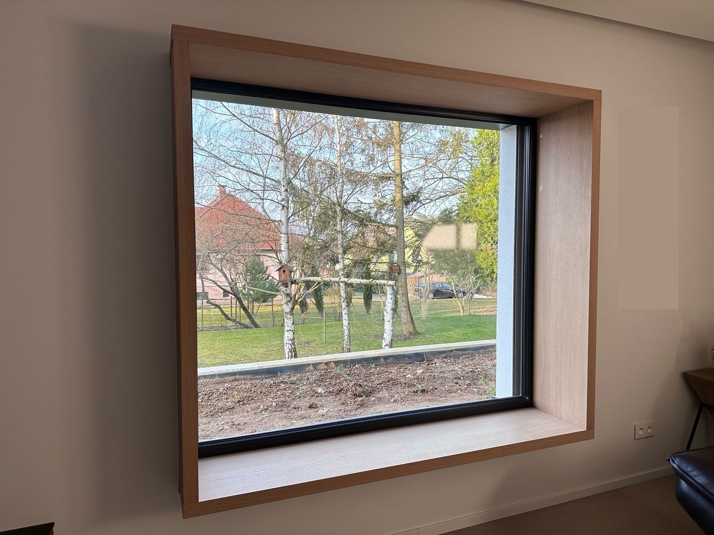 Banquette de fenêtre : caisson profond en décor chêne habillant une grande baie à cadre noir, assise sur l’appui