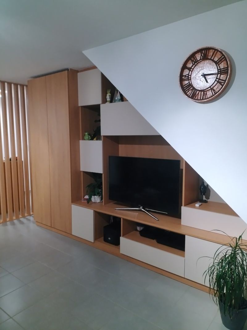 Meuble TV sur mesure sous l'escalier : colonnes et niches en chêne et blanc qui suivent la pente, claustra de lattes bois à gauche